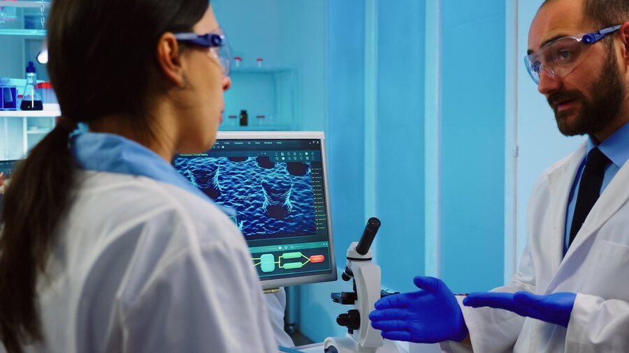 Químicos profesionales que analizan el desarrollo de vacunas mediante una pantalla táctil en un laboratorio equipado con exceso de trabajo